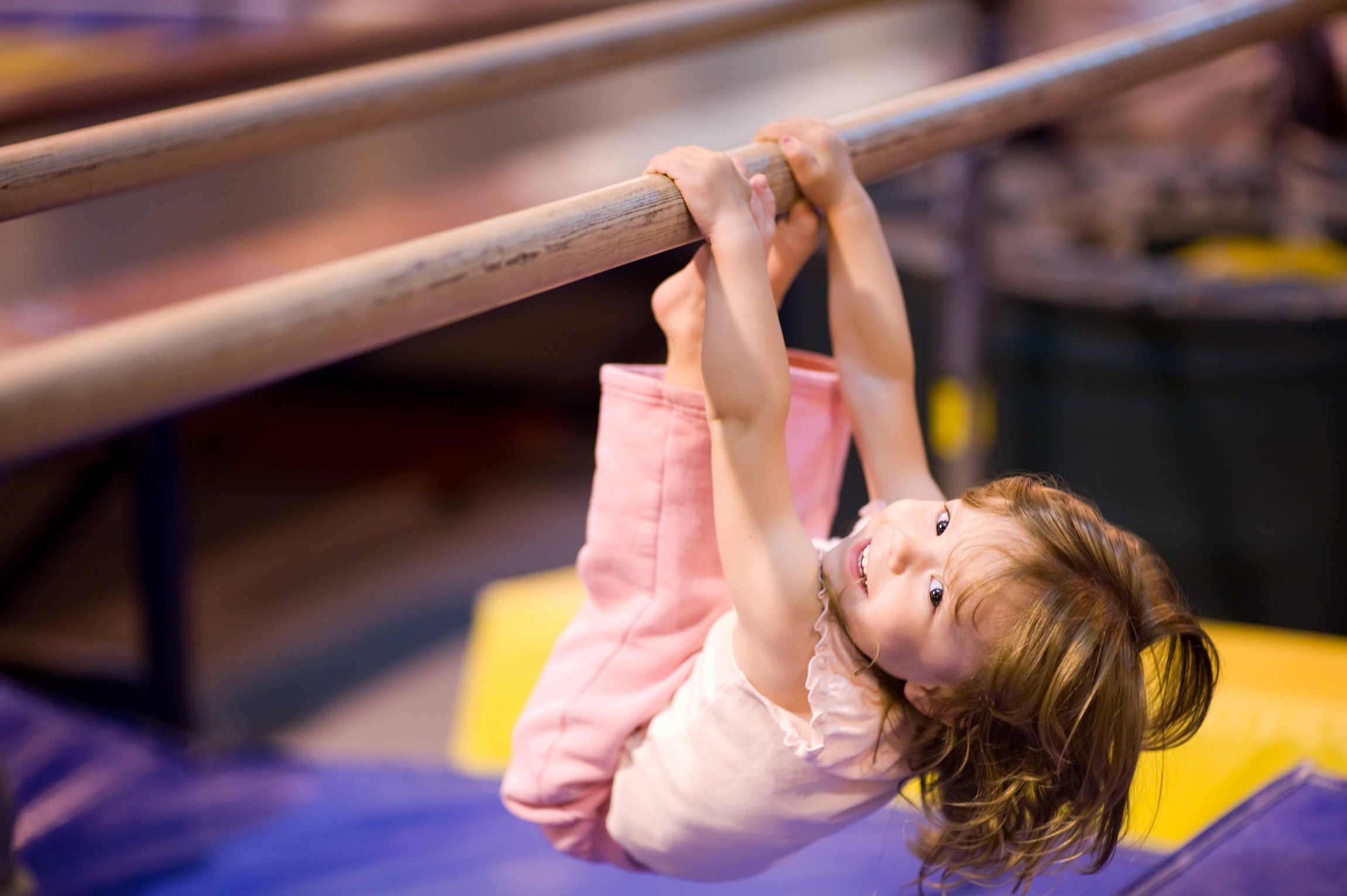 young girl hanging from a gymnastics bar