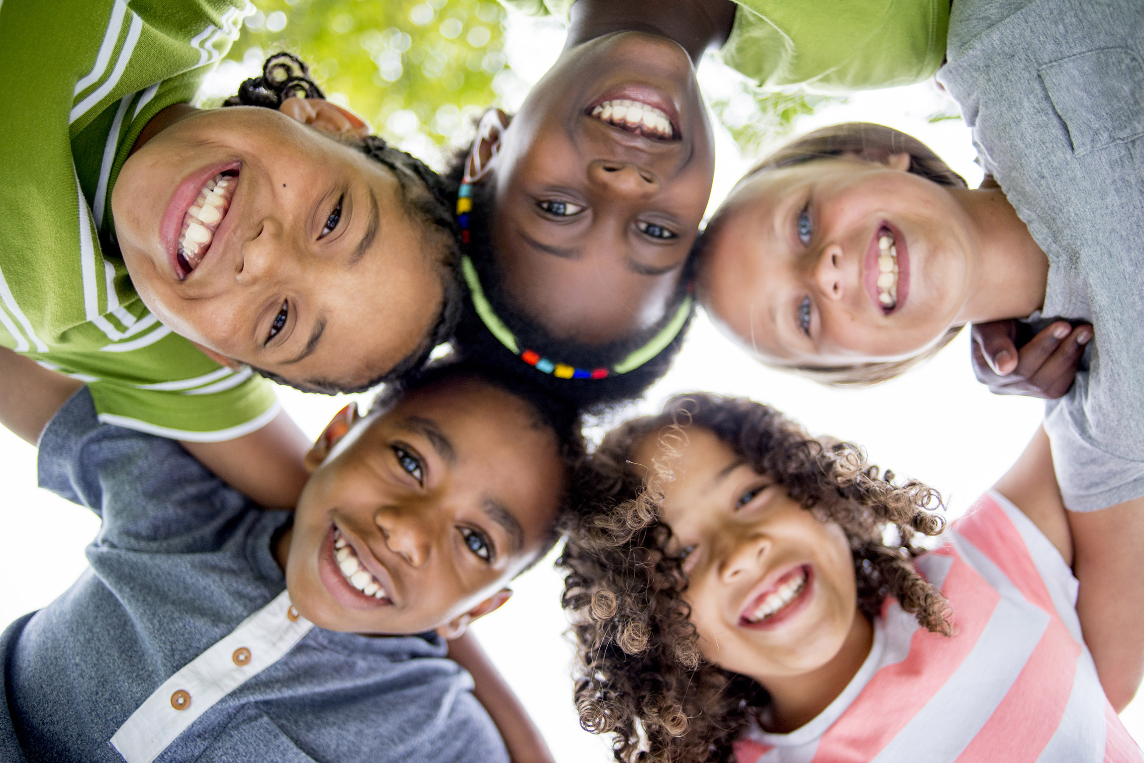 children in a group huddle, smiling down on the camera