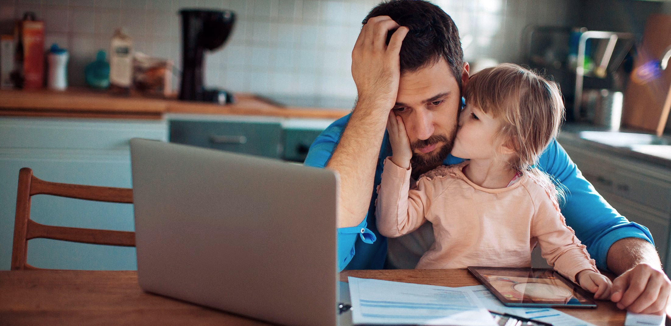 father stressed looking at computer and paperwork while young daughter comforts him