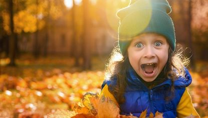young girl playing in fall leaves with a look of "Wow"