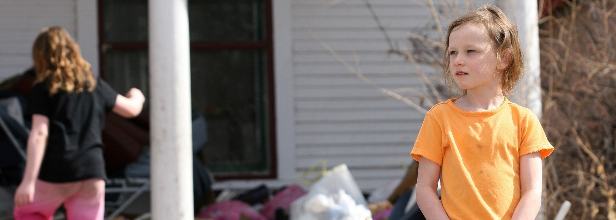 child standing outside looking unsure, in a messy yard