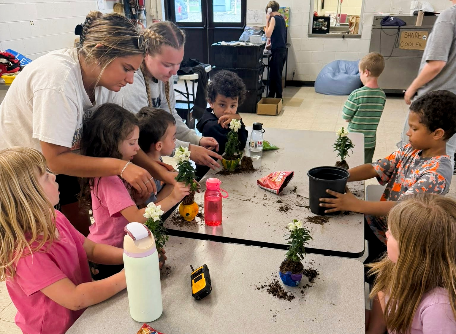 kids at table working on a craft with staff helpers assisting them