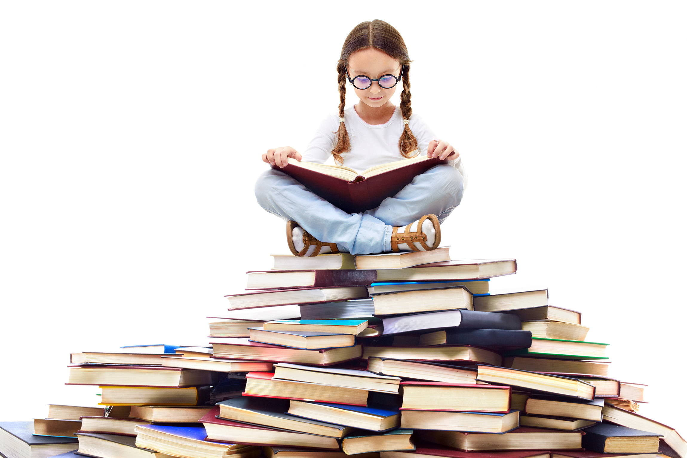 girl with glasses and pigtails sitting on a large pyramid-shaped pile of books, reading a book