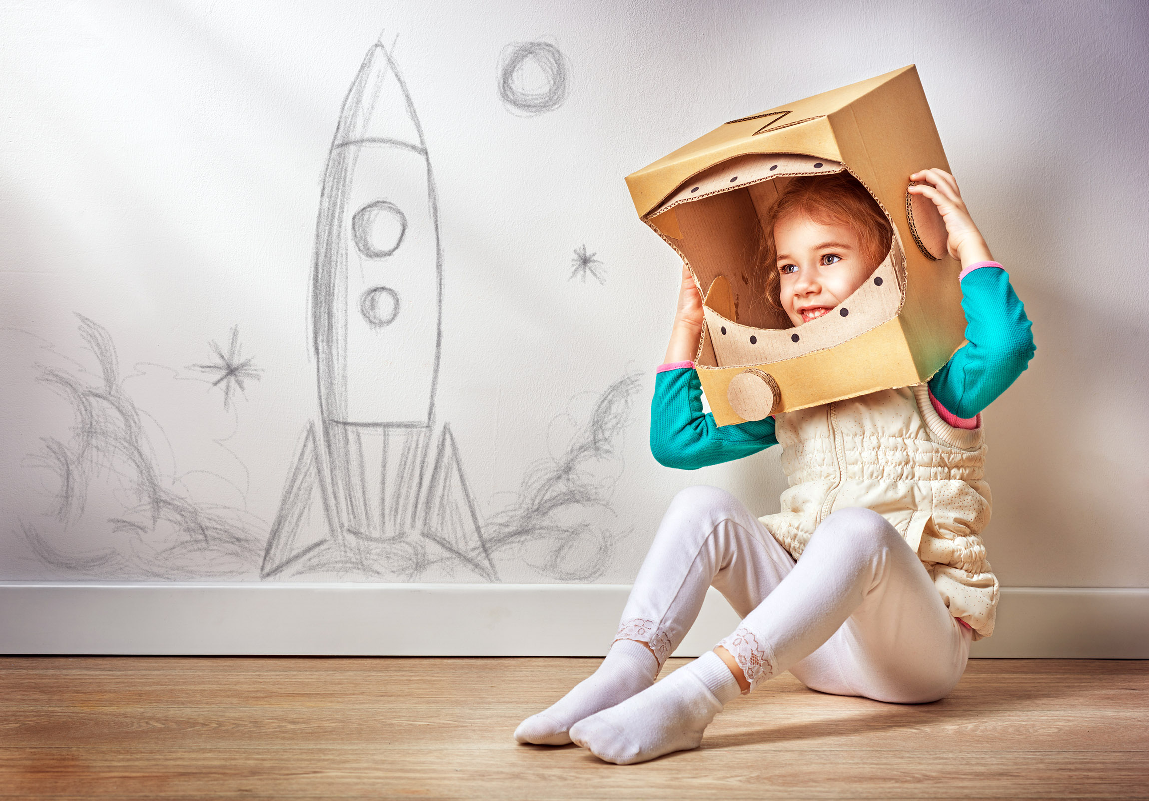 child sitting next to a drawing of a rocket wearing a homemade helmet