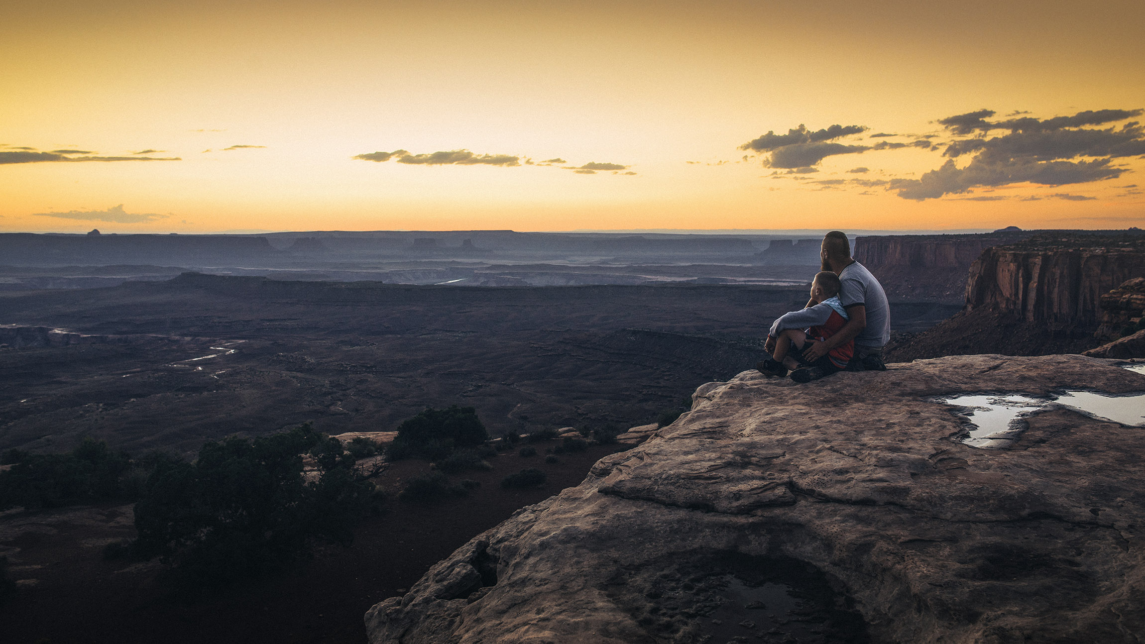 man and child sitting atop a large canyon looking at the biew