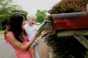 a woman and child smiling while taking a book out of a mailbox
