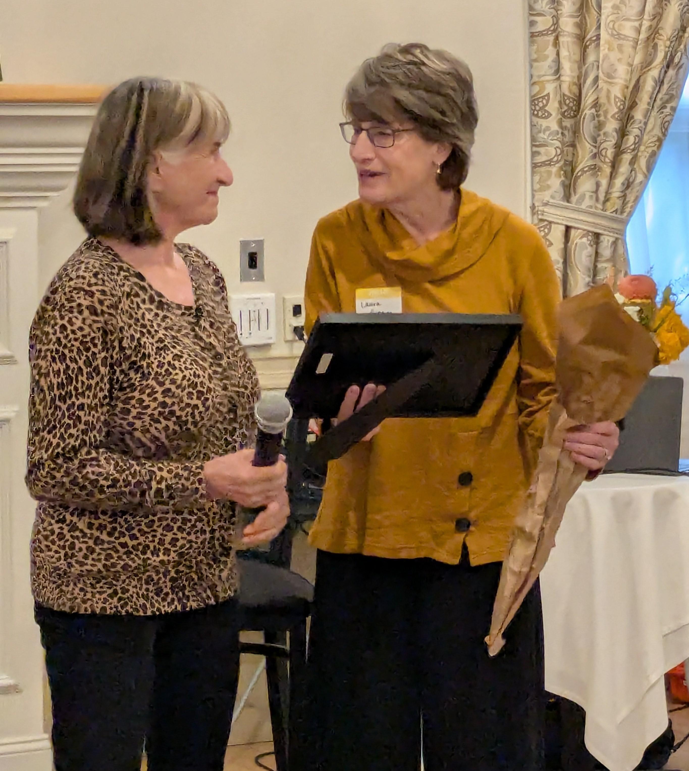Joann Fenton presents Laura Gingras, the 2026 Ken Jue Award winner, with flowers and a plaque 
