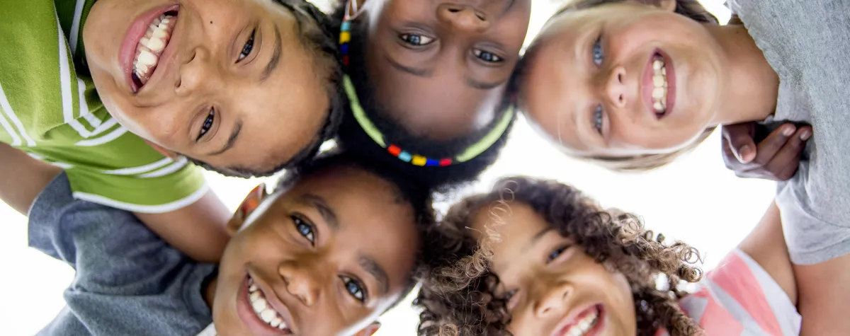 children in a group huddle, smiling down at the camera