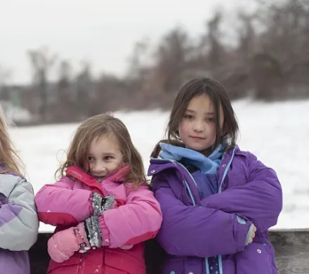 three girls in winter coats standing with arms crossed