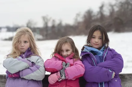 three girls in winter coats standing with arms crossed