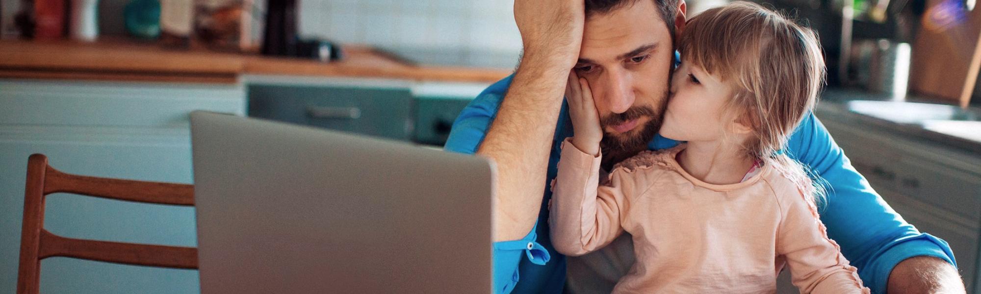 father stressed looking at computer and paperwork while young daughter comforts him