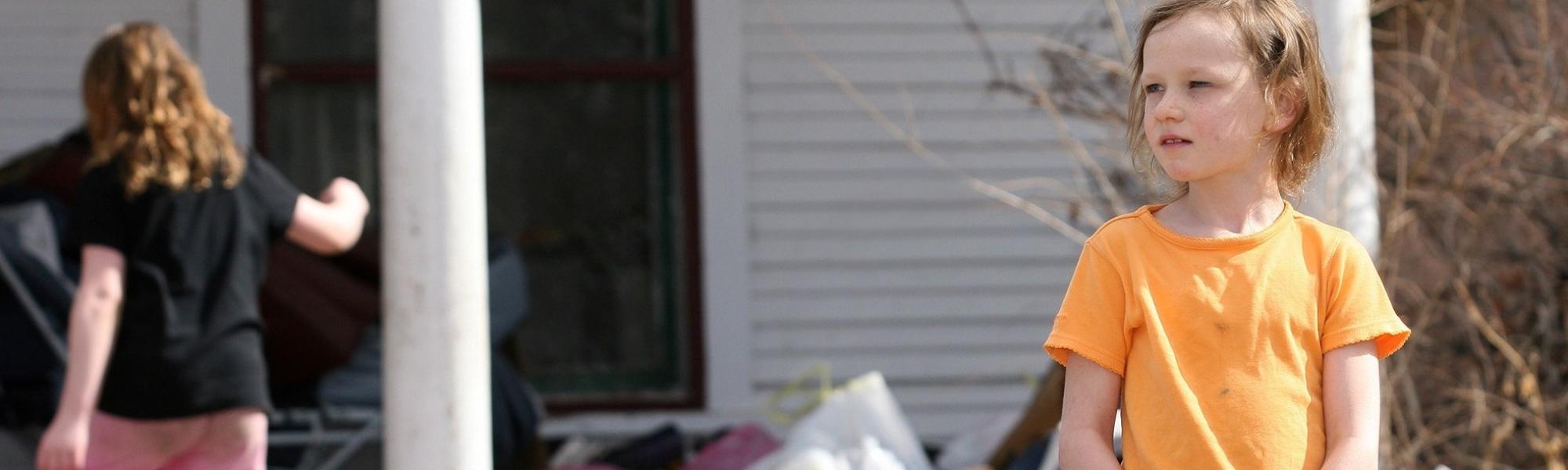 child standing outside looking unsure, in a messy yard