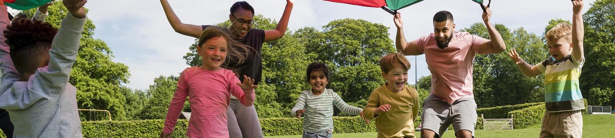 children and adults happily playing in a field with a parachute