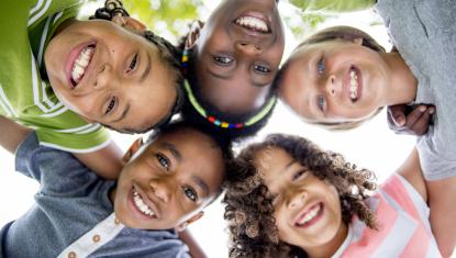 children in a group huddle, smiling down on the camera